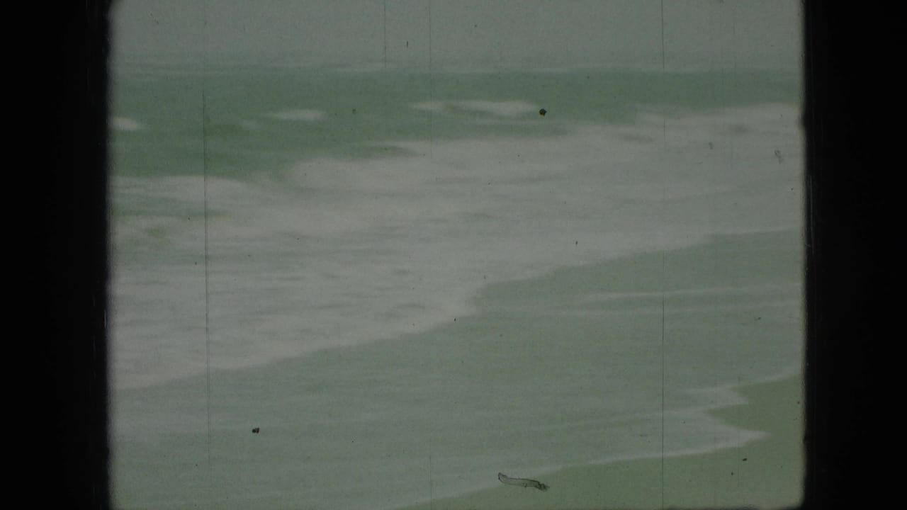 1968 8mm home-movie frame showing pale greenish-blue water and white foam bands, with dark gate edges and visible film wear.