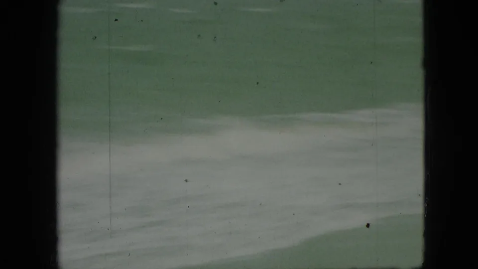 1968 8mm frame of greenish water with pale foam streaks, framed by black film edges and light archival scratches.