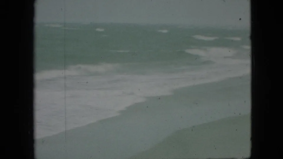 1968 8mm home-movie frame showing a broad white foam pattern over green water, with grain, scratches, and dark frame borders visible.