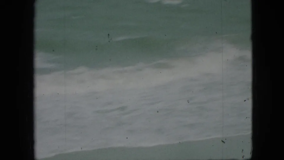 1968 8mm frame showing white foam and rippled green water, with black frame edges and surface marks from the film scan.