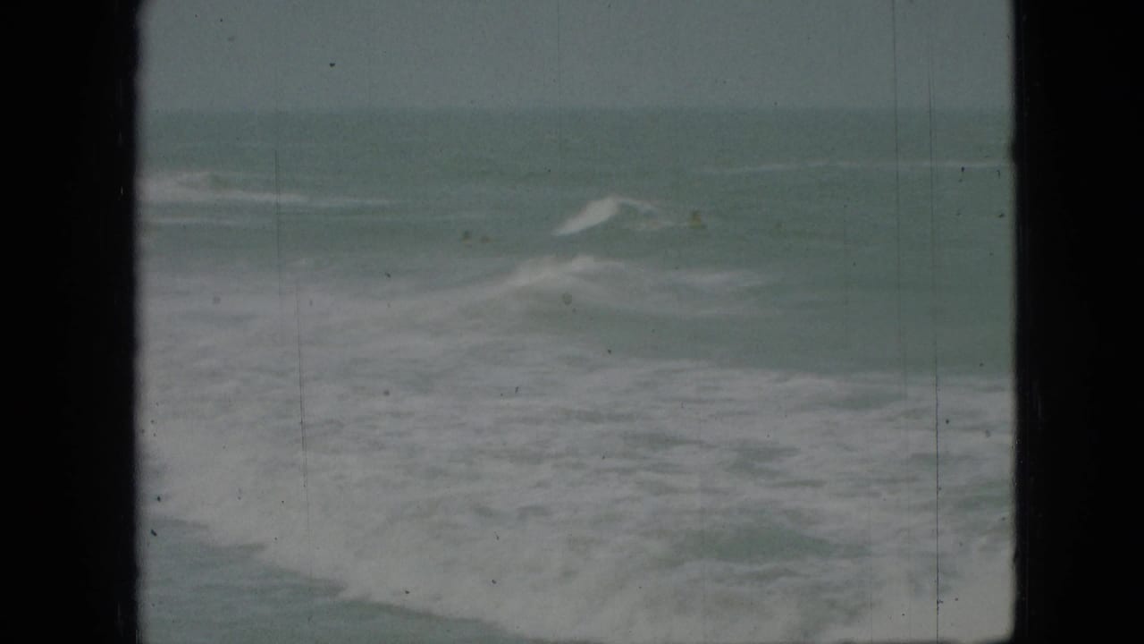 Breaking waves and white foam under a muted gray-green sky.