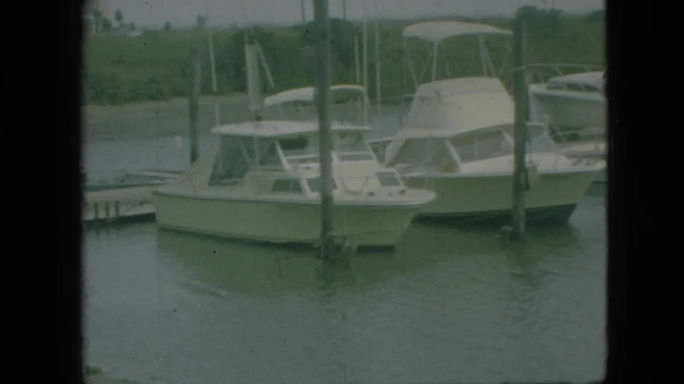 1968 Branson, Missouri marina view with white fiberglass cabin boats tied near dock pilings under an overcast sky.