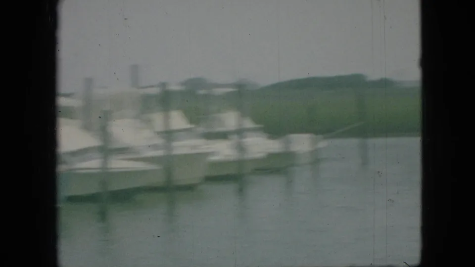Blurred 8mm marina frame from Branson, Missouri with moored boats, dock pilings, calm water, and low shoreline beyond.