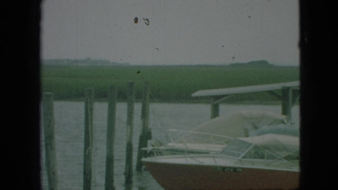 1968 Branson, Missouri 8mm frame showing a covered dock, pilings, and a small pleasure boat viewed through dark vertical window or cabin edges.