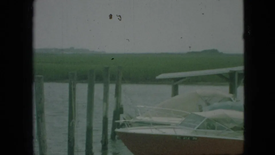 1968 Branson, Missouri 8mm frame showing a covered dock, pilings, and a small pleasure boat viewed through dark vertical window or cabin edges.