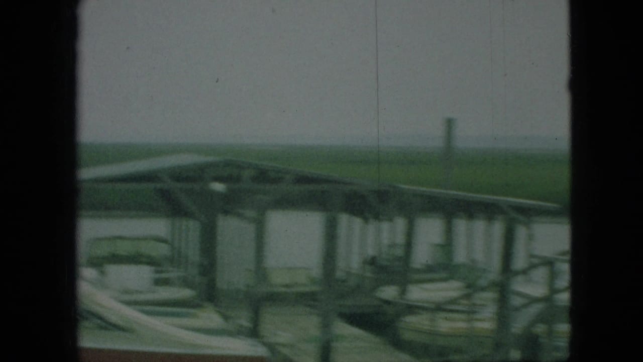 1968 Branson, Missouri 8mm frame with docked boats under a covered pier, partially blocked by a dark vertical window or cabin edge.