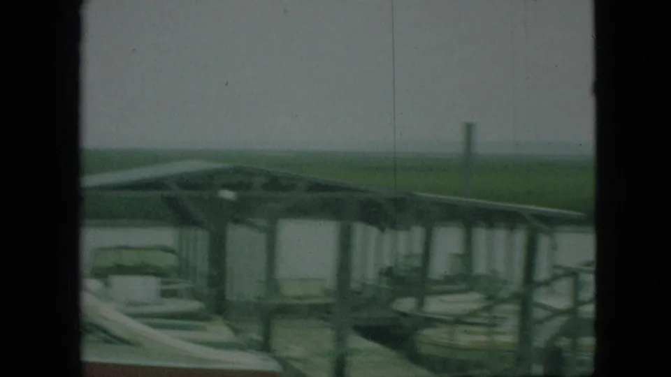 1968 Branson, Missouri 8mm frame with docked boats under a covered pier, partially blocked by a dark vertical window or cabin edge.