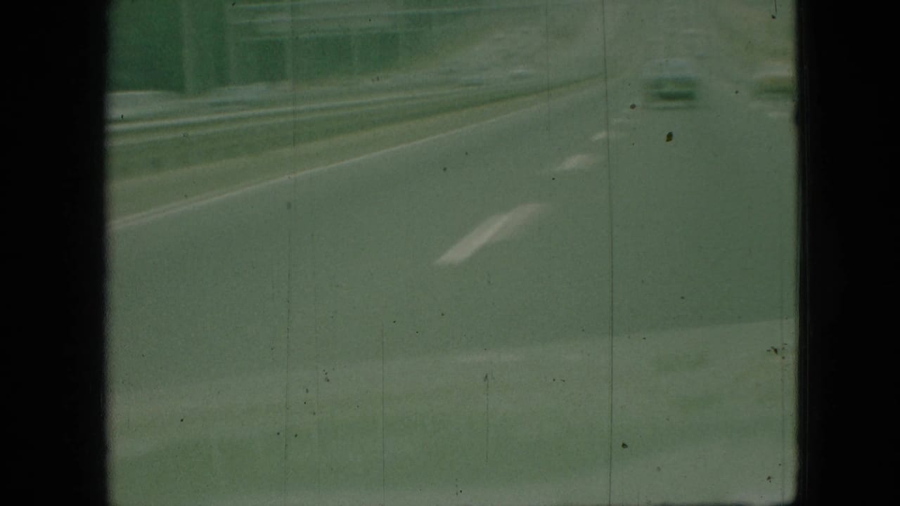 Highway lane and guardrail viewed through a greenish, grainy car-window perspective.