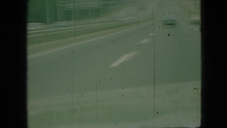 1968 Branson, Missouri road-travel frame with a soft green cast, showing highway pavement, lane markings, guardrails, and a small distant vehicle.