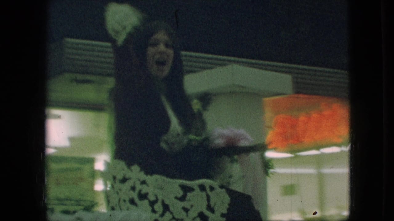 Woman in a dark coat waves from a decorated parade vehicle near storefront signs.