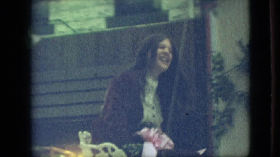 A smiling woman rides on a decorated parade vehicle with flowers in front of a street-facing building, matching the clip's Branson parade context.
