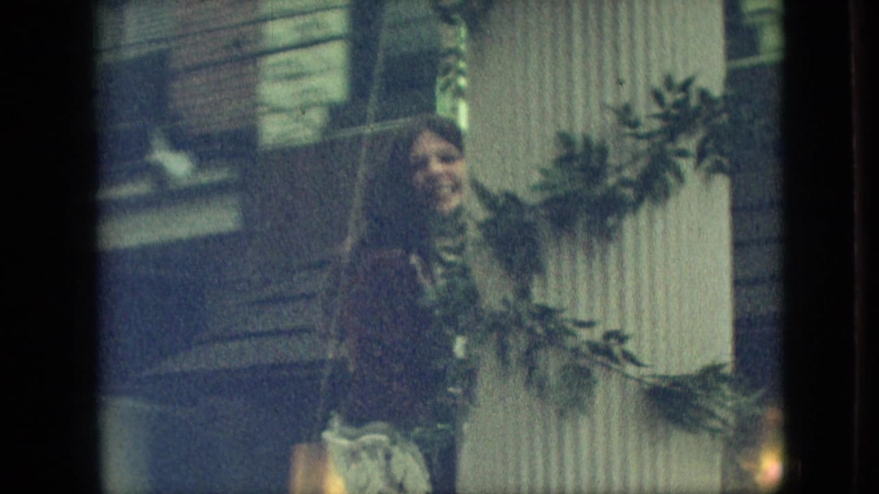 In the supplied 1968 Branson, Missouri footage, a woman in a dark dress stands near a white pillar wrapped with green garland on a parade float.