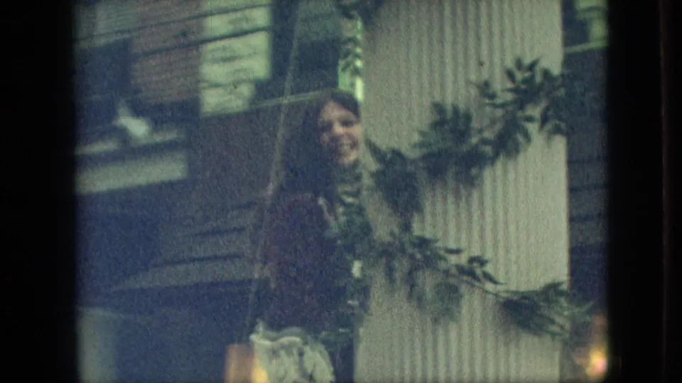 In the supplied 1968 Branson, Missouri footage, a woman in a dark dress stands near a white pillar wrapped with green garland on a parade float.