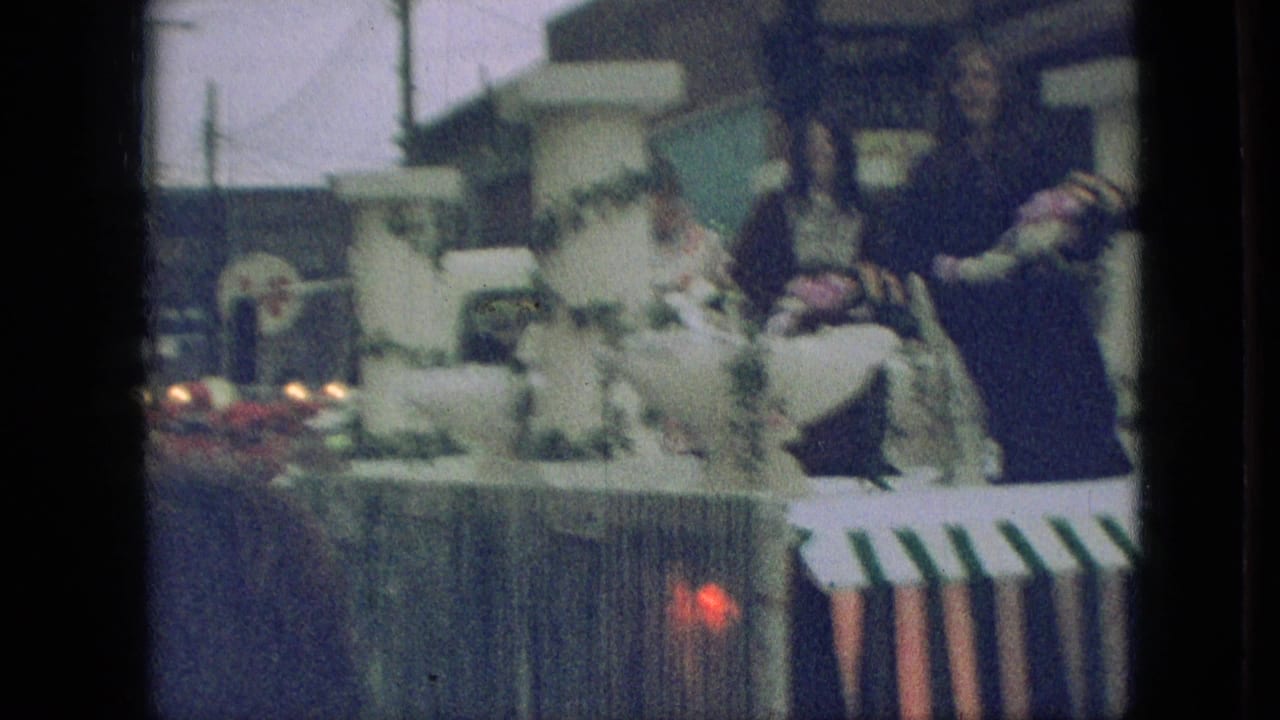 1968 Branson, Missouri parade view of a decorated float with women in formal attire, white columns, floral trim, and a red light or reflection near the camera.