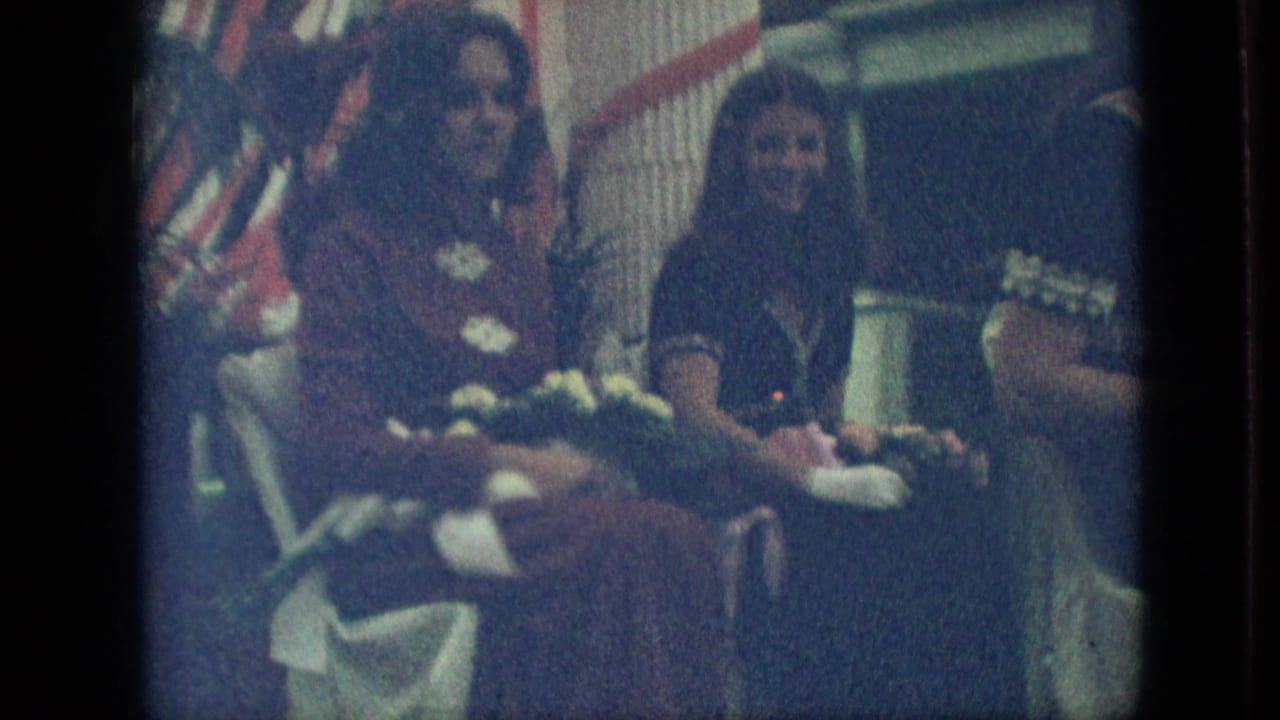 Closer view of women seated on the float beside flowers, columns, and red-and-white trim.