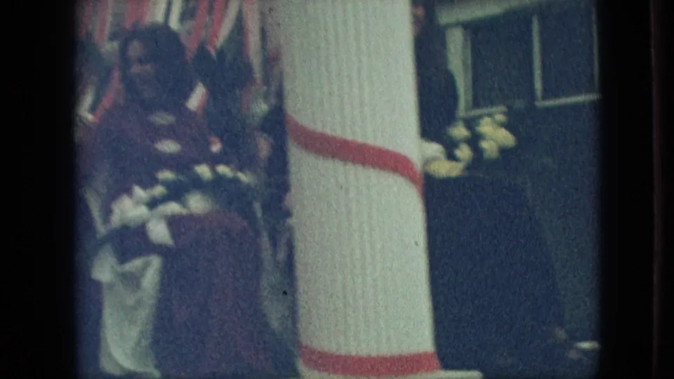 1968 Branson, Missouri parade footage showing a woman on the decorated float near a white column, flower trim, and dark background panels as the float passes.