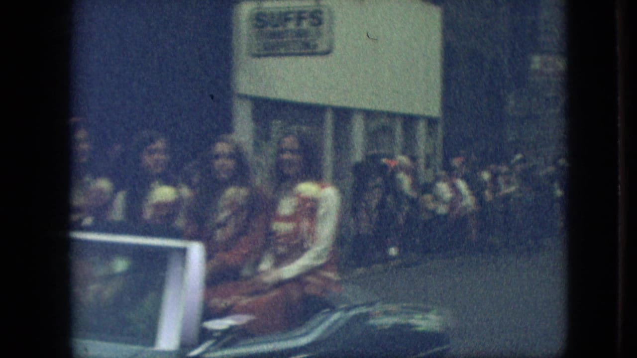 In Branson, Missouri, a 1968 home-movie frame shows a parade convertible with women seated inside as spectators line the sidewalk near a storefront sign.