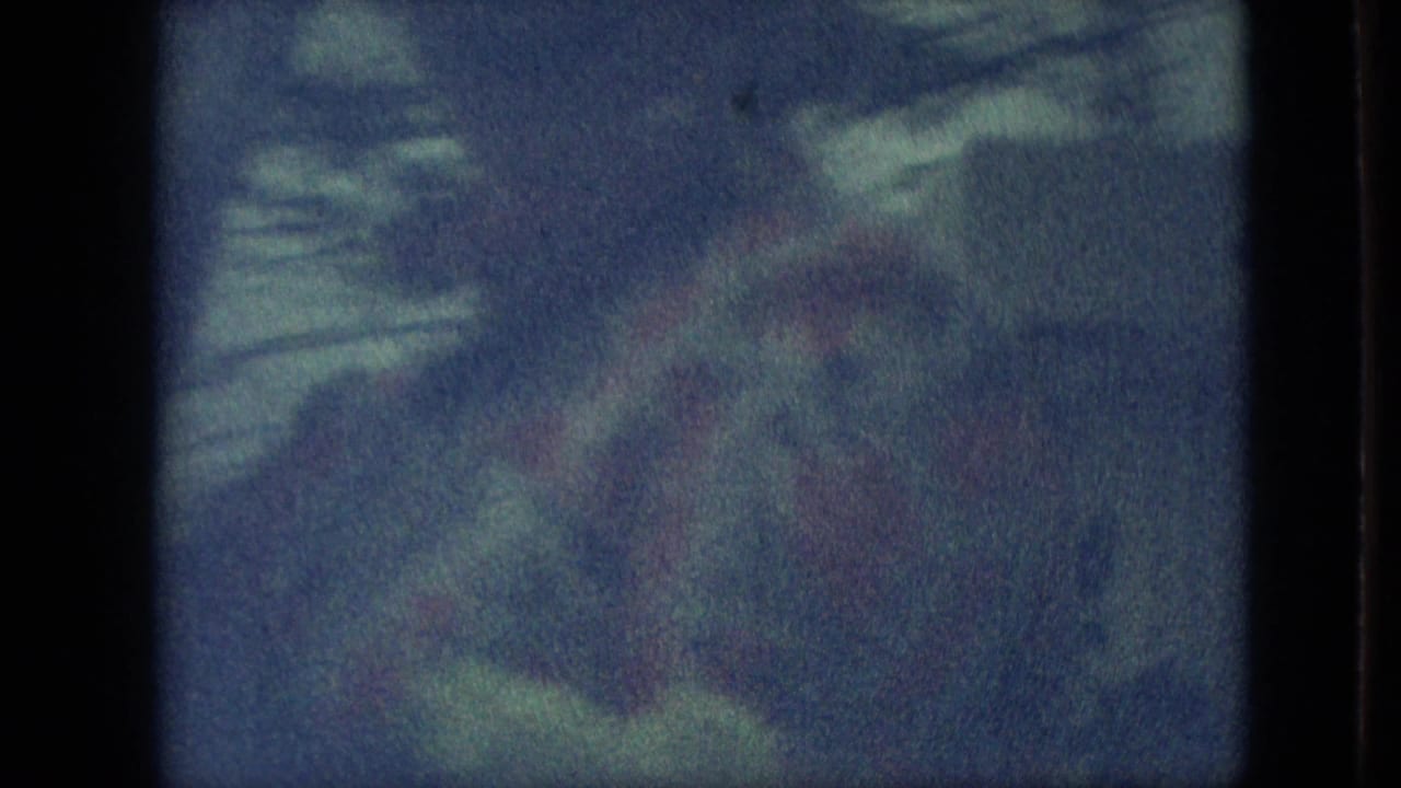 A blurred 8mm frame appears to show parade participants or nearby spectators, with indistinct faces and clothing softened by motion and exposure.