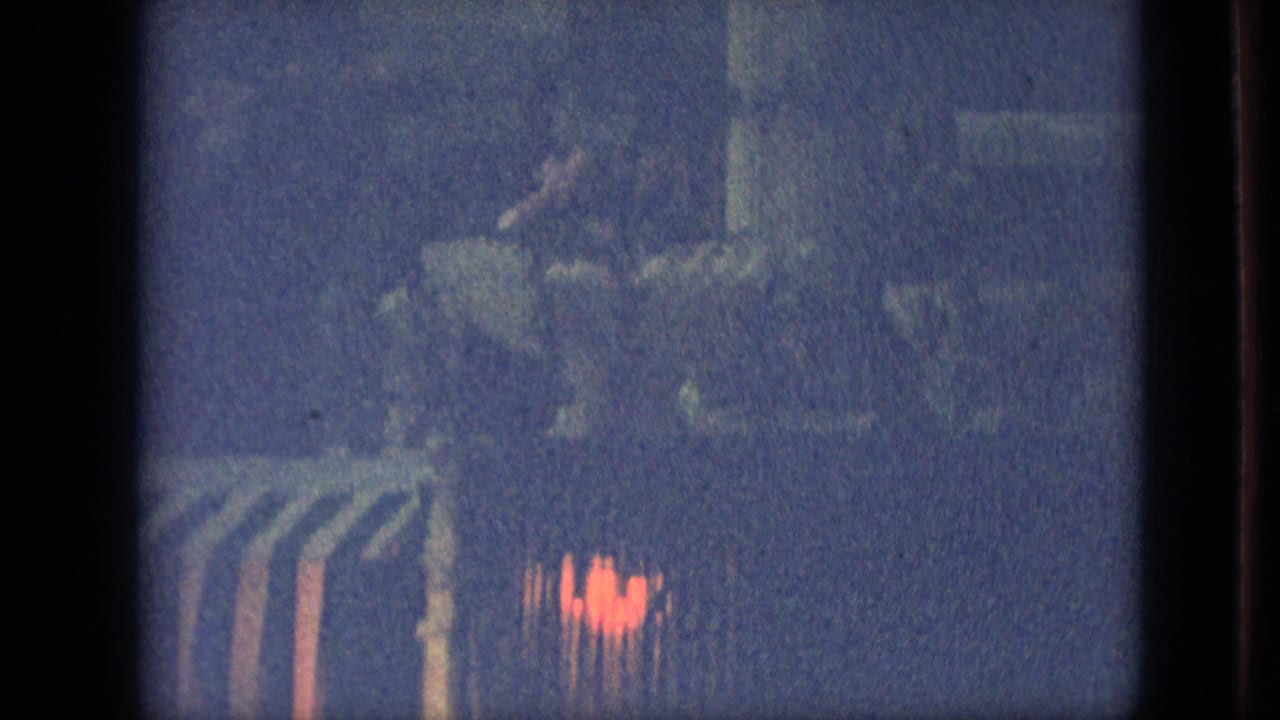 Branson, Missouri 1968 home-movie frame showing a barely visible nighttime parade float or structure with red decorative light under heavy grain and blue exposure.