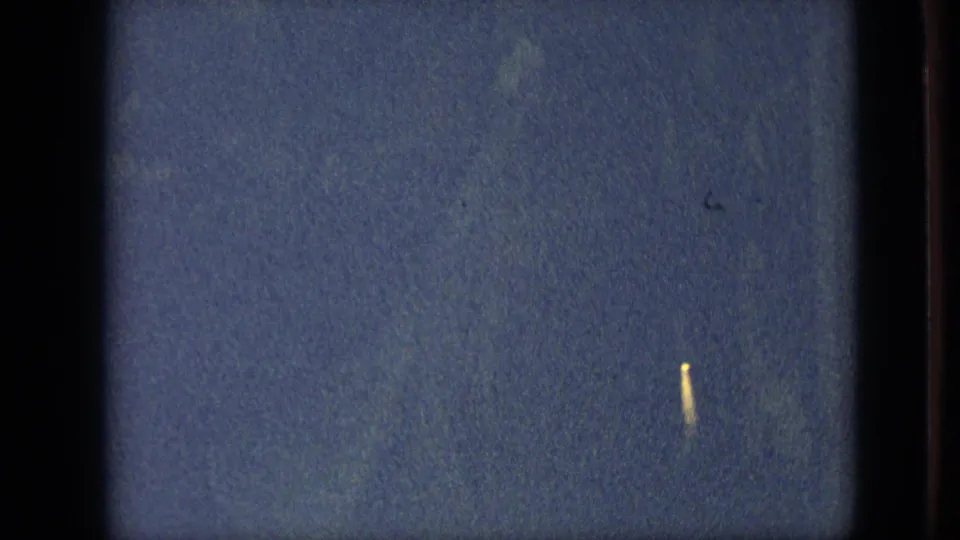 Branson, Missouri 1968 nighttime parade frame reduced mostly to blue darkness, film gate edges, grain, and a small yellow light streak on the right.