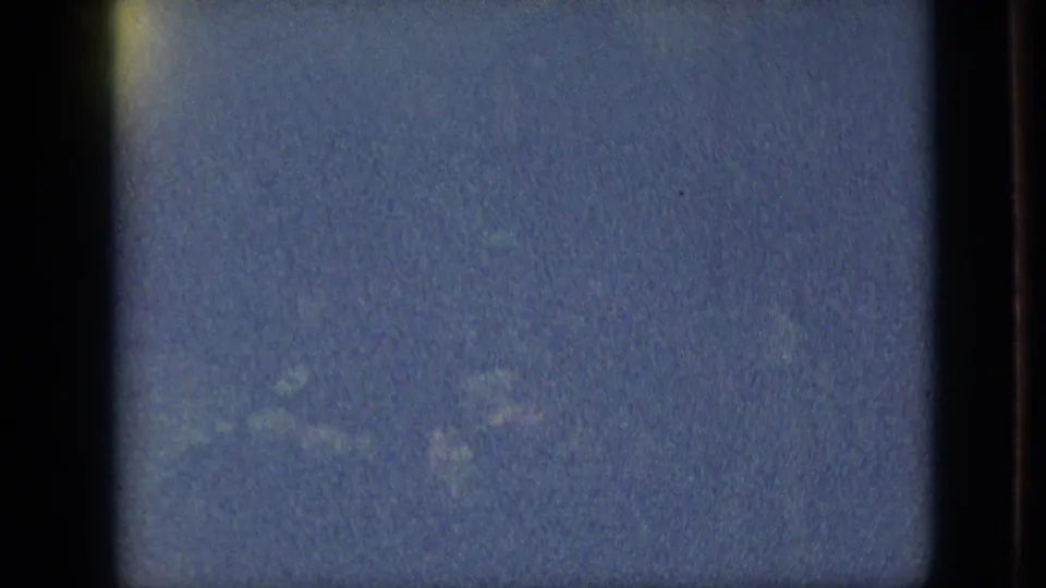 Underexposed 1968 Branson night-parade frame with soft blue grain, faint indistinct forms, and the rounded edge of the 8mm film image.