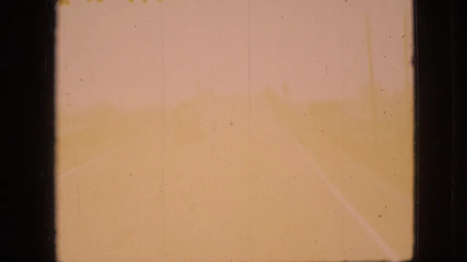 Faded 8mm frame where a roadway begins to appear through yellow-orange color degradation, with a lane line and soft film texture visible.