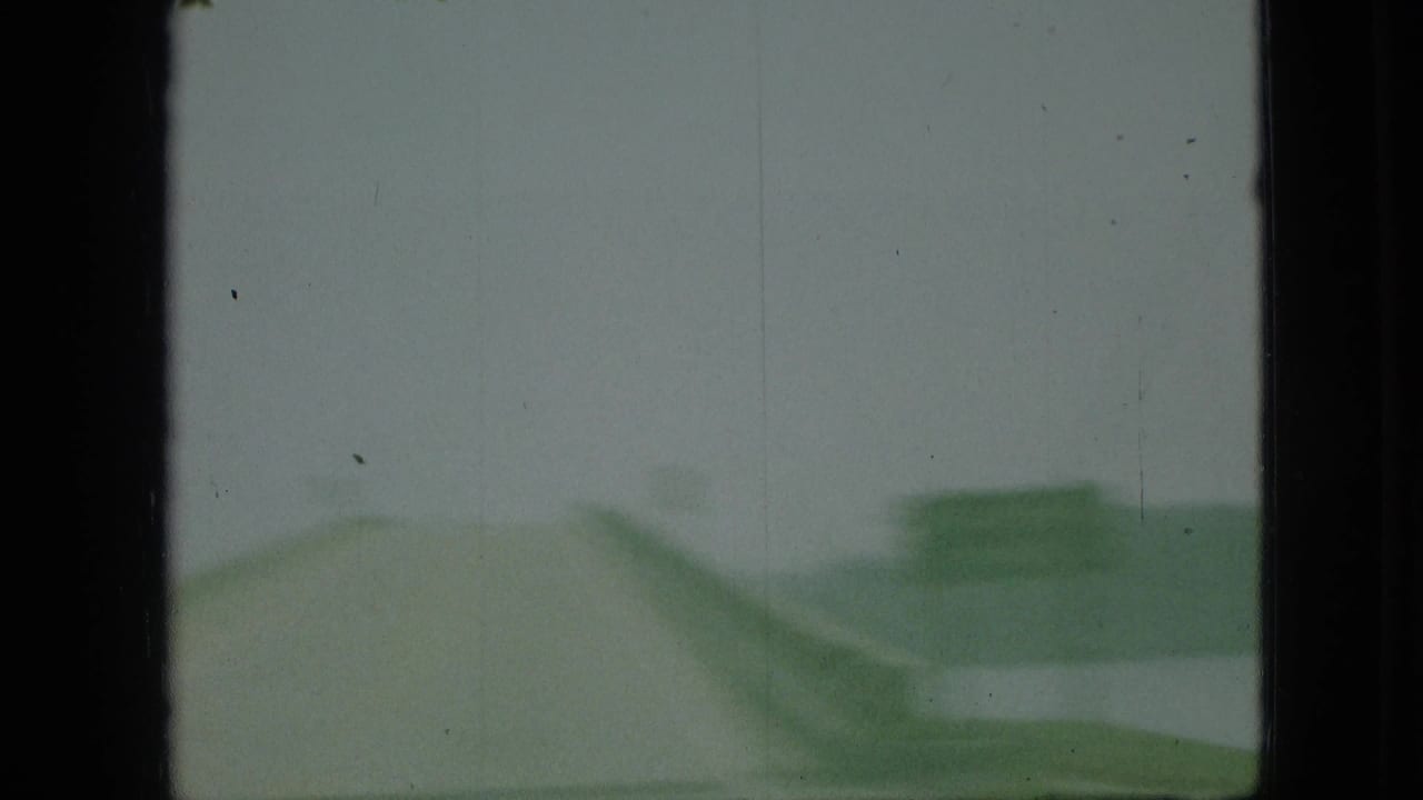 1968 Branson, Missouri 8mm frame showing a blurred moving-car view with an overcast sky, green roadside form, and heavy film-frame borders.