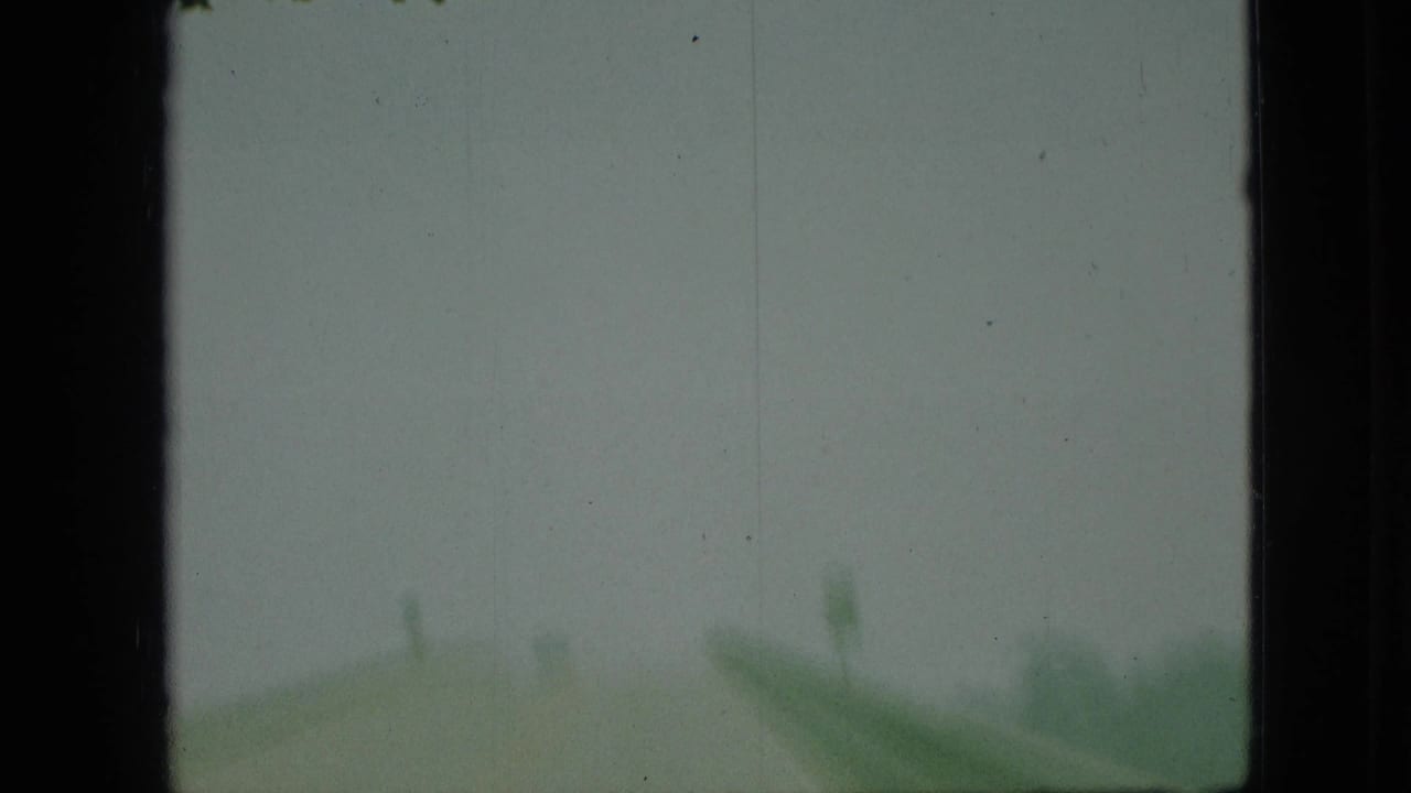 Blurred roadside view with a green sign-like shape under a gray sky.