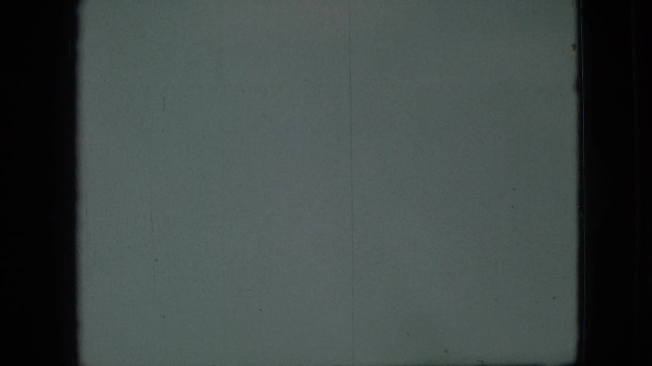 1968 Branson, Missouri 8mm frame showing a very soft gray-green view through dark vertical frame edges, with grain and faint surface marks dominating the scene.