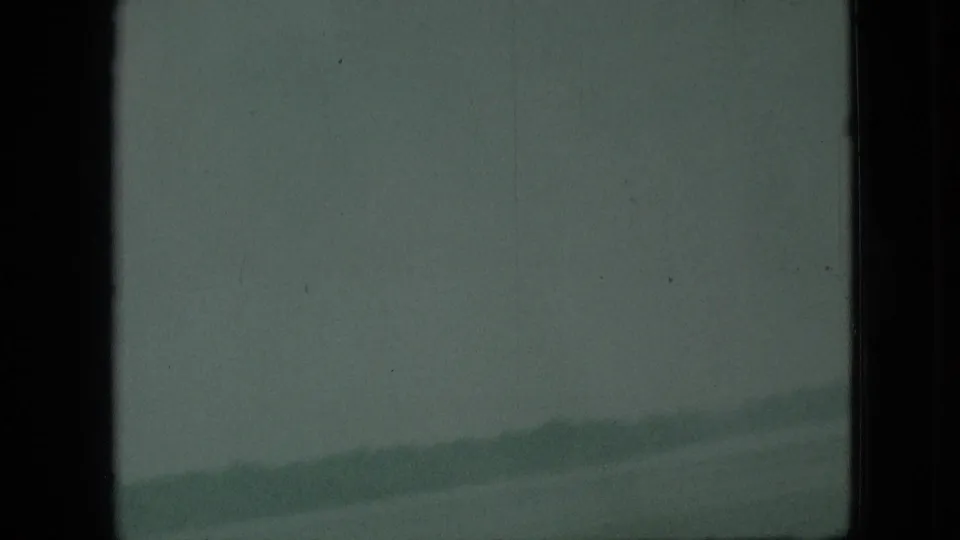 1968 Branson, Missouri travel frame with pale water or sky, a faint distant shoreline or hill line, dark vertical borders, and visible 8mm grain.