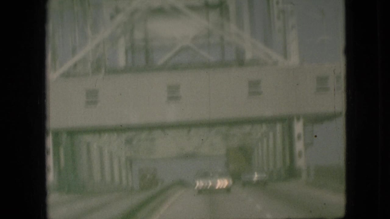 Forward-looking 1968 Branson, Missouri road view beneath a steel truss bridge, with cars visible ahead through the windshield or window framing.