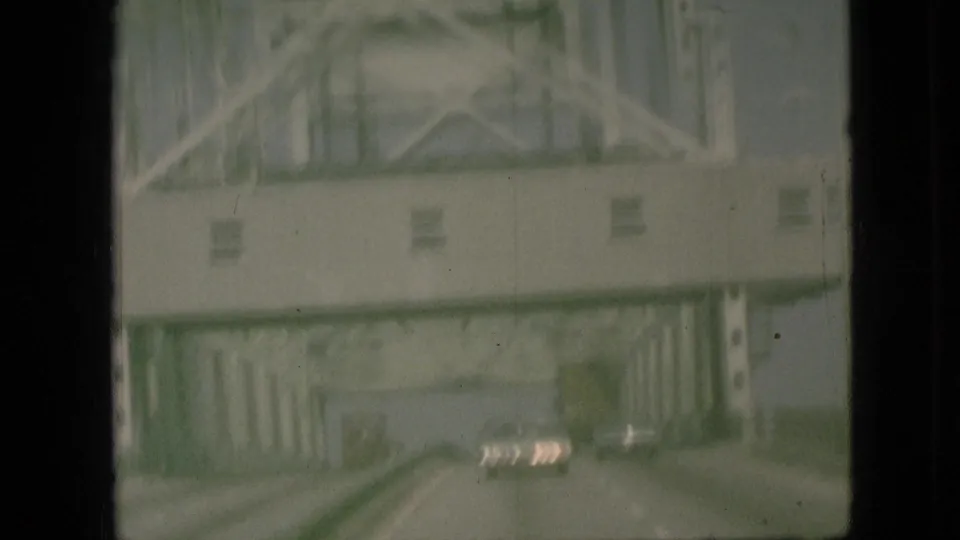 Forward-looking 1968 Branson, Missouri road view beneath a steel truss bridge, with cars visible ahead through the windshield or window framing.