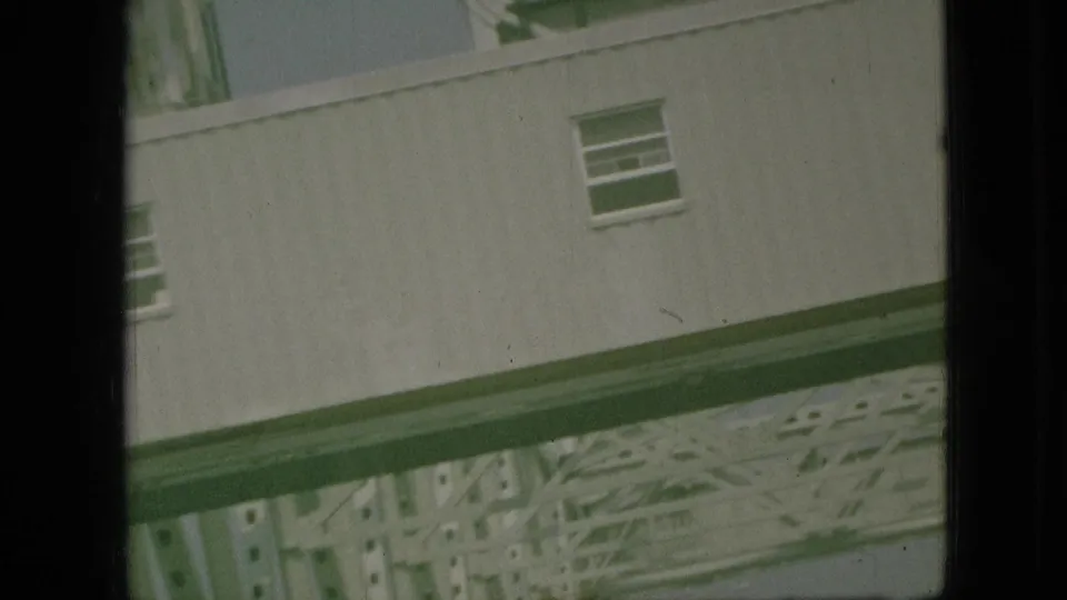 1968 Branson, Missouri home-movie frame showing a tilted pale building wall and structural framework glimpsed through dark window edges.