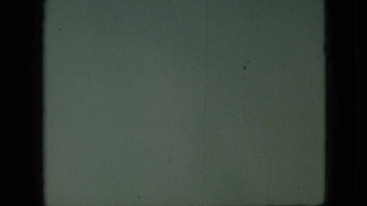 Green-tinted 8mm frame with little visible subject detail, bordered by dark vertical edges and faint film marks.
