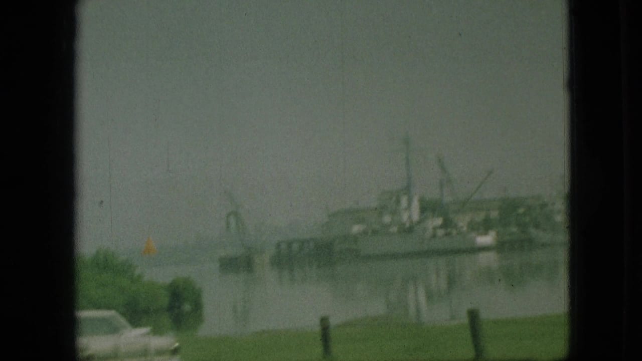 Waterfront view with a docked vessel or marina structure, grass, a car roof, and an American flag.