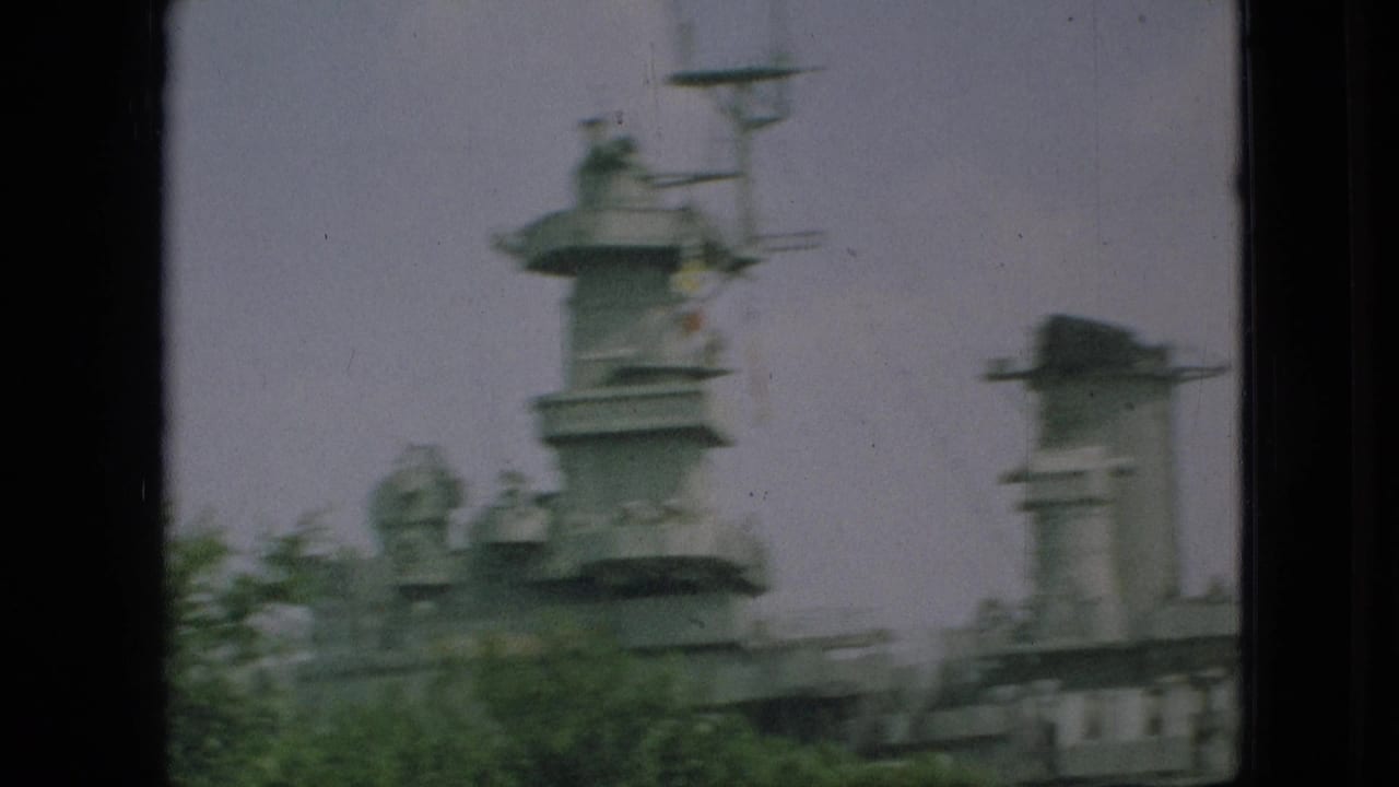 1968 Branson, Missouri home-movie frame showing a gray naval superstructure with mast and turret-like forms seen through foliage and dark vertical borders.