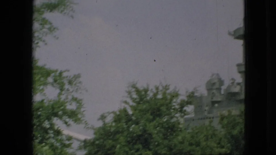 A partially blocked 1968 Branson view of a gray battleship or naval memorial structure seen beyond leafy trees and a dark window-like divider.