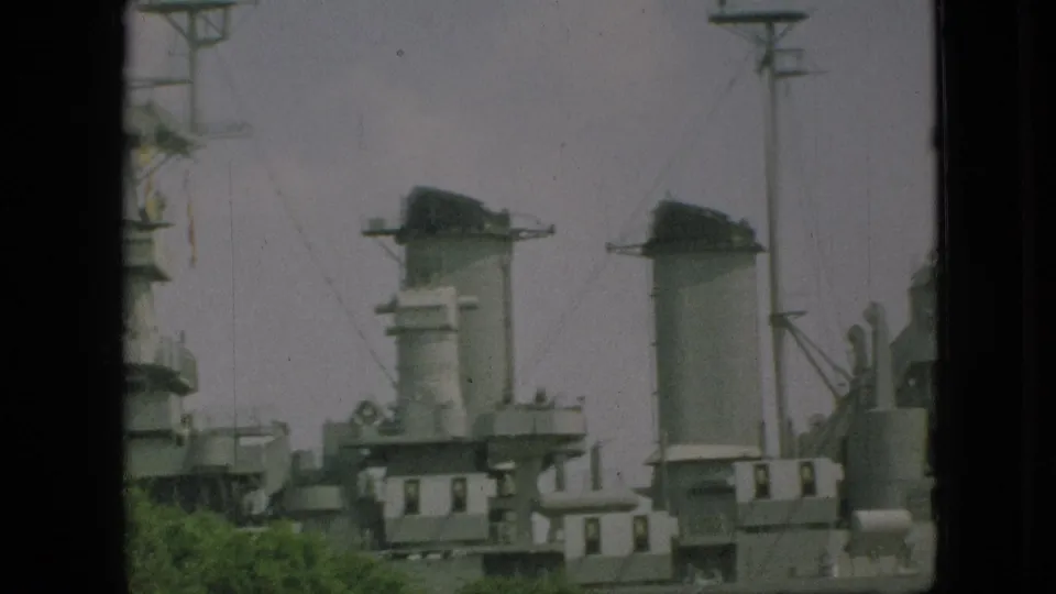 1968 Branson home-movie frame showing gray naval deck structures, tall housing forms, rigging lines, and trees along the lower edge.