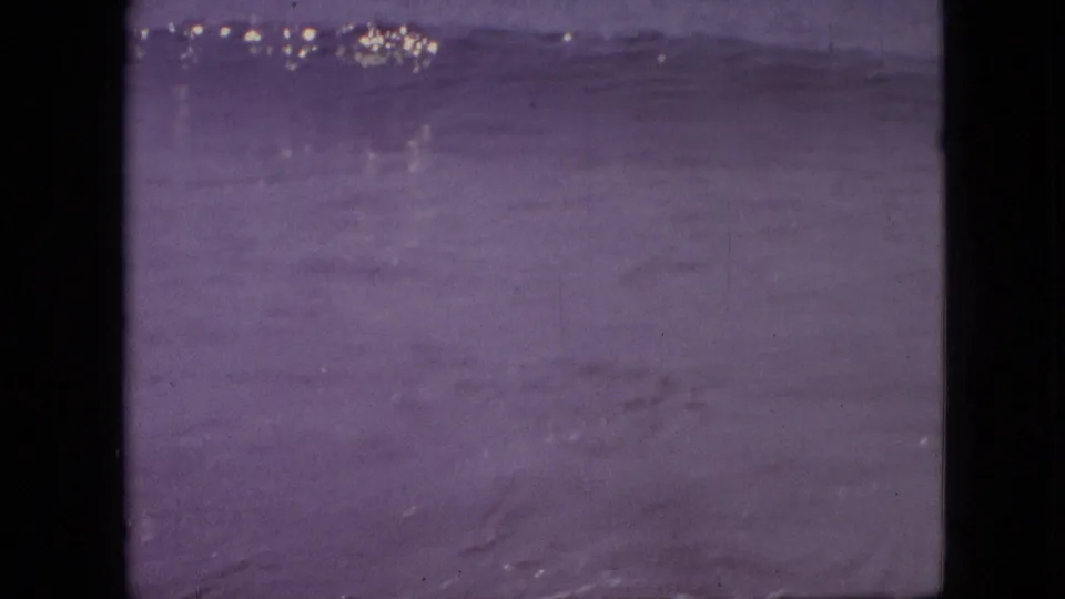 1960s 8mm home-movie frame showing open water and a faint horizon with purple color shift, scratches, and visible film edge borders.