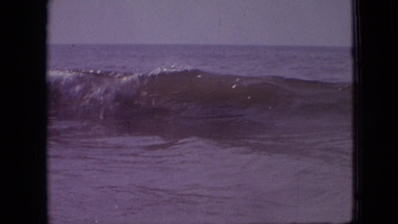 A wave rises near the horizon with dark film borders on either side.