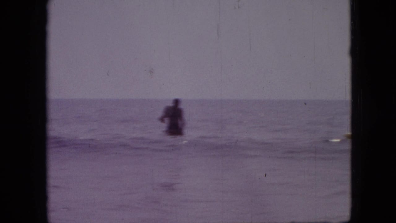 A distant person stands or swims in open water in this 1968 8mm home-movie frame recorded as Branson, Missouri, with soft focus and purple film tint.