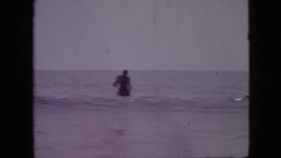 A distant person stands or swims in open water in this 1968 8mm home-movie frame recorded as Branson, Missouri, with soft focus and purple film tint.