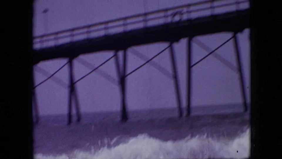 1968 8mm home-movie frame, cataloged as Branson, Missouri, showing a foamy wave rolling beneath dark pier beams and supports with open water in the background.