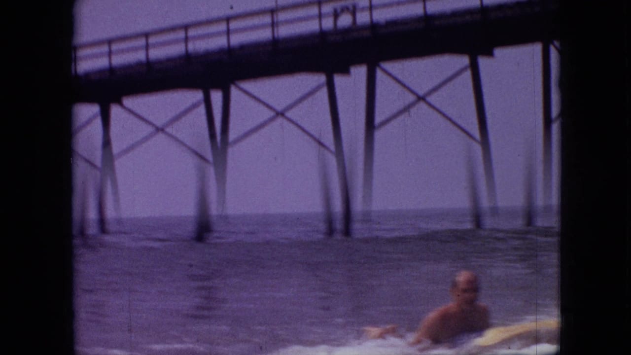 Adult male surfer paddling near pier supports in choppy water.