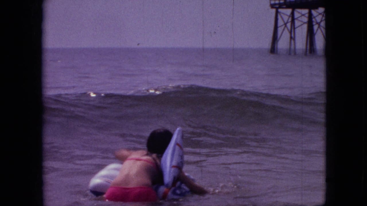 1968 8mm home-movie frame, cataloged as Branson, Missouri, showing a surfer or swimmer with a board in the foreground while a darker wave forms in front of a distant pier structure.