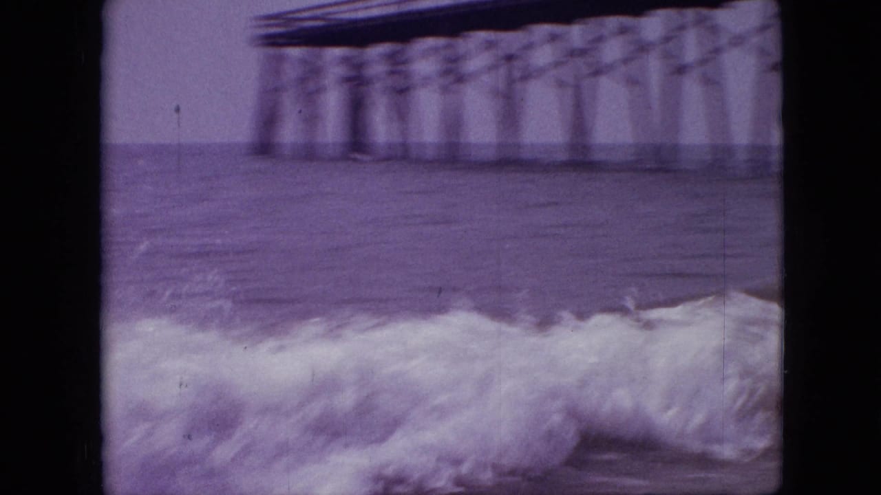 1968 8mm home-movie frame, cataloged as Branson, Missouri, showing a foamy foreground wave with a blurred pier span and supports across the water behind it.