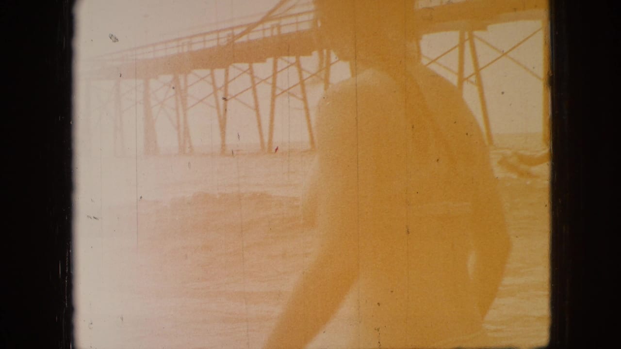 Faded 1968 8mm home-movie frame from Branson, Missouri, showing a bridge or elevated structure near water with heavy yellow exposure and film-edge borders.