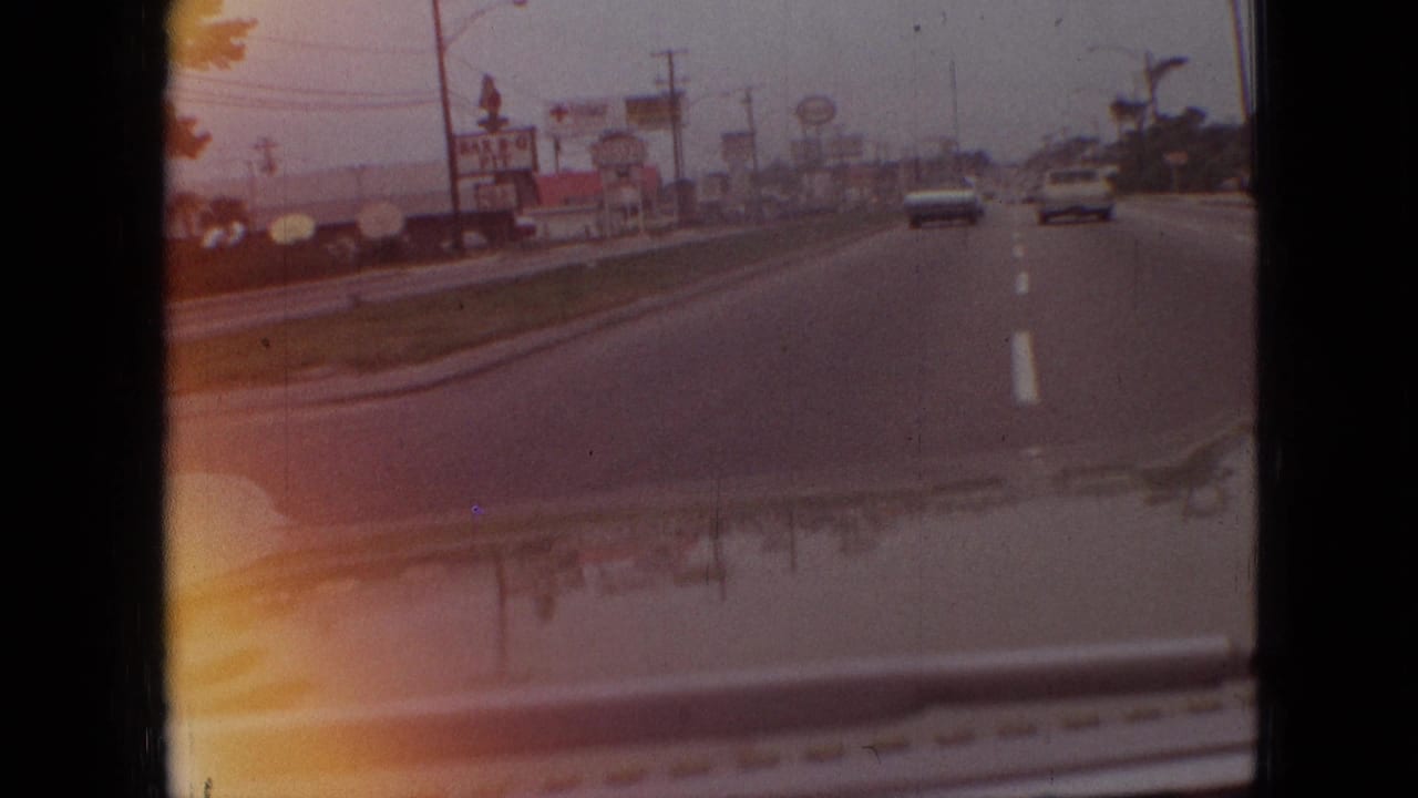 1968 Branson, Missouri road scene from a moving vehicle, with period cars ahead, roadside signs including a Bar-B-Q Pit sign, lane markings, and visible 8mm frame edges.