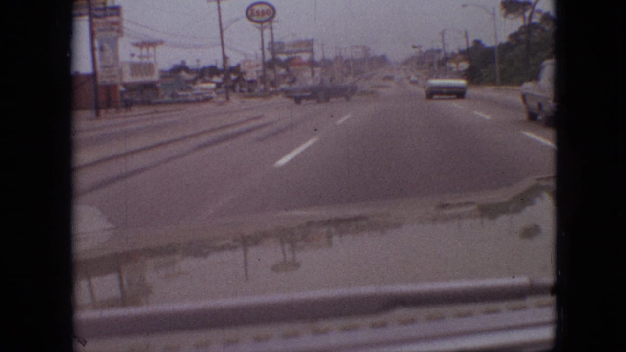 1968 Branson, Missouri moving-car footage showing a commercial roadside, classic traffic, lane markings, a vehicle at the right edge, and the filming car's hood in the foreground.