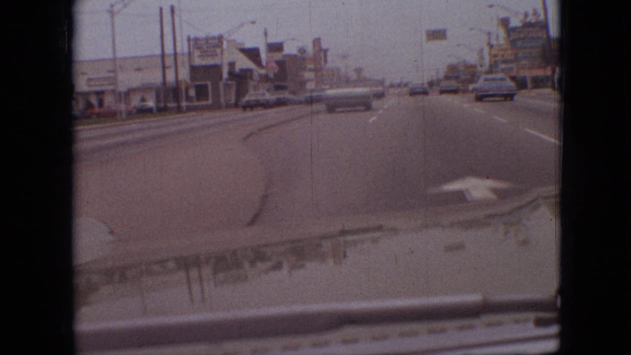 View from a moving car along a multi-lane road with traffic and roadside businesses.